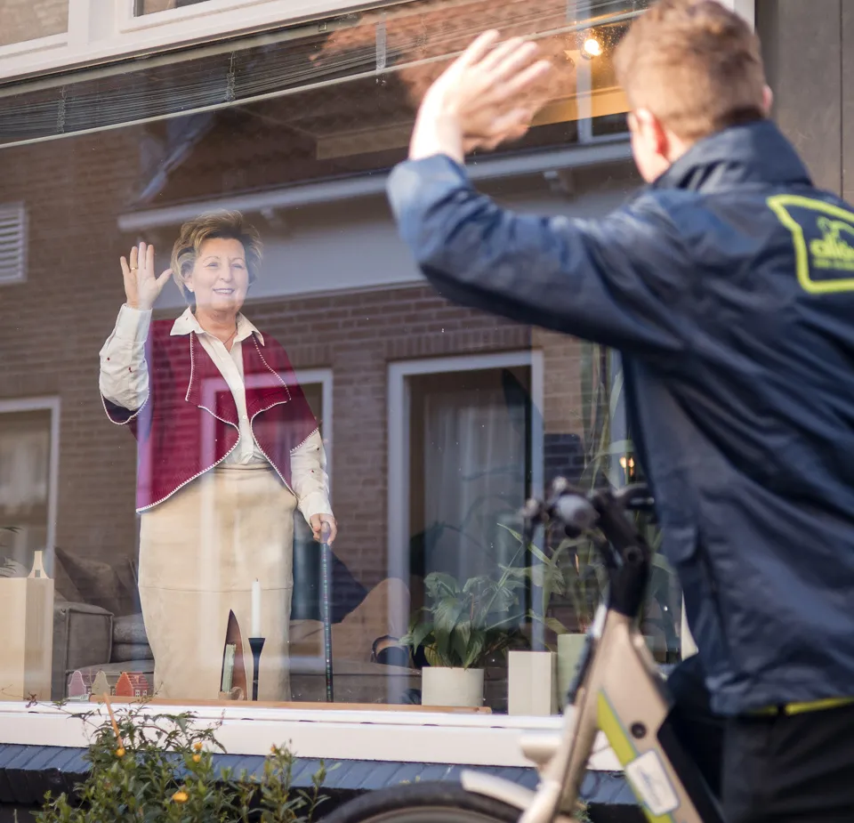 medewerker zwaait van buiten naar client binnen wijkverpleging verwijzers