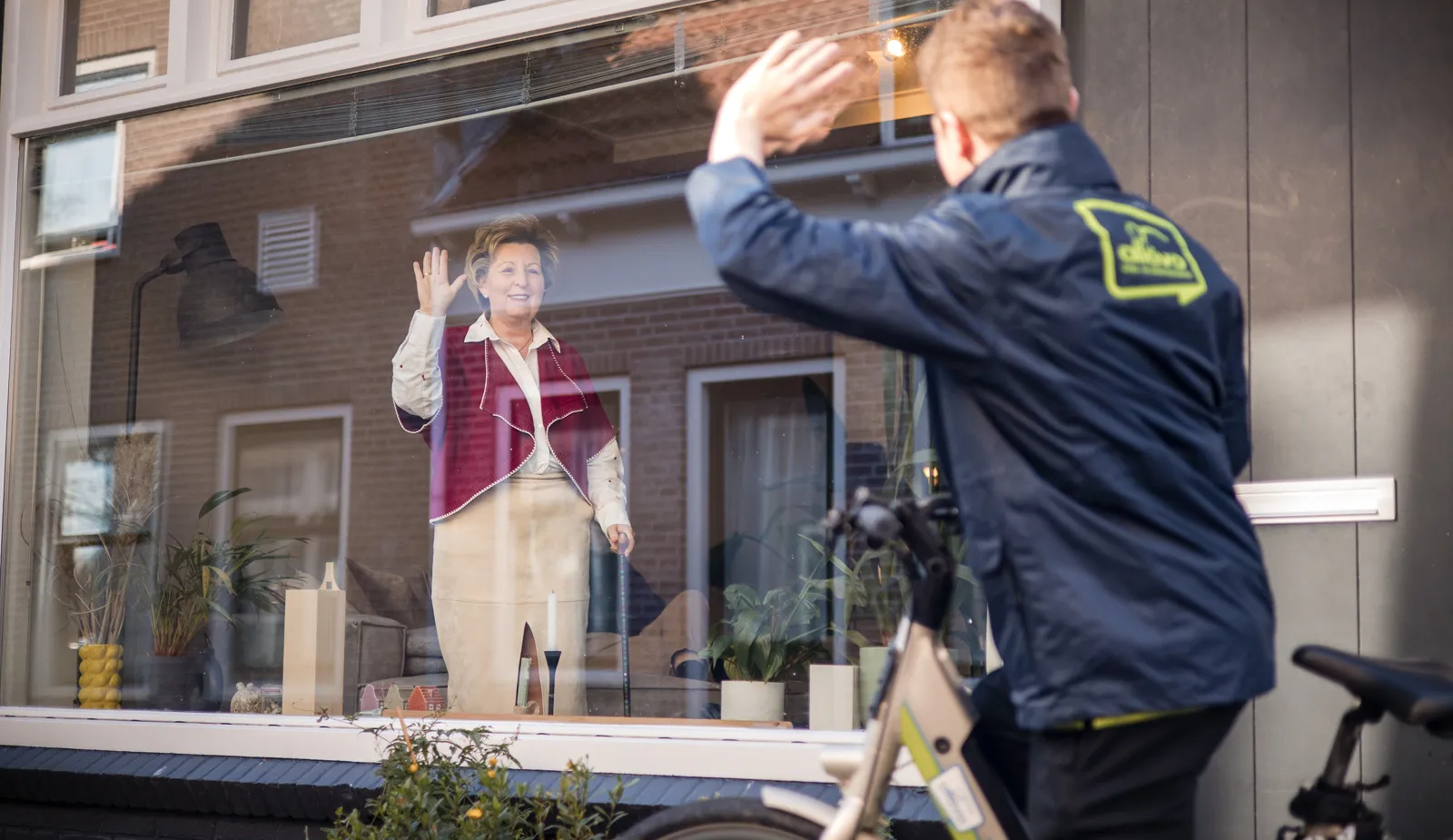 medewerker zwaait van buiten naar client binnen wijkverpleging verwijzers