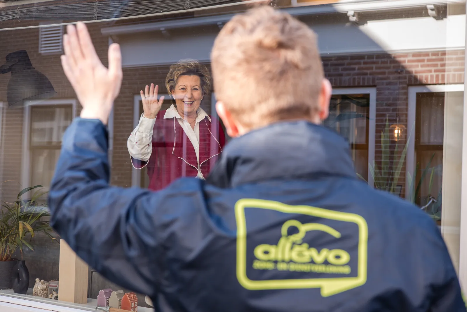 Medewerker zwaait naar cliënt in Allévo jas.